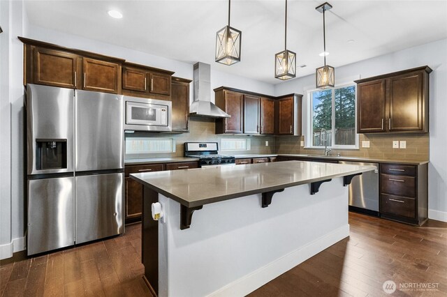 kitchen with stainless steel appliances, tasteful backsplash, dark wood-style floors, and wall chimney exhaust hood