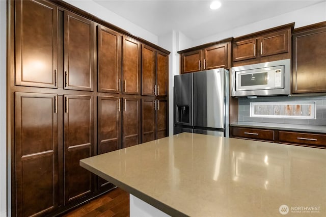 kitchen with stainless steel appliances, tasteful backsplash, dark brown cabinets, and dark wood-style flooring