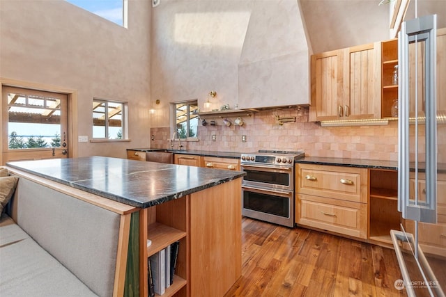 kitchen with a kitchen island, light brown cabinetry, decorative backsplash, range with two ovens, and light hardwood / wood-style floors