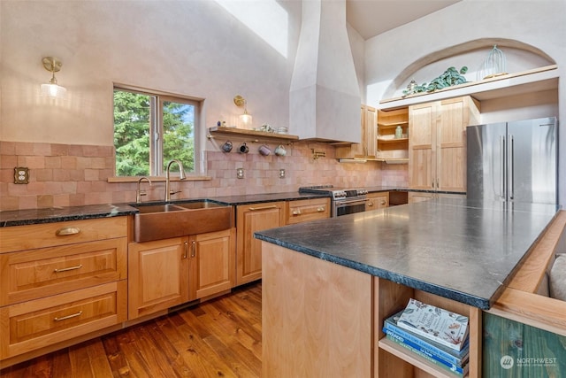 kitchen with sink, wood-type flooring, appliances with stainless steel finishes, a towering ceiling, and backsplash