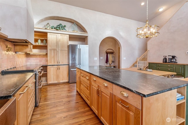 kitchen featuring a kitchen island, appliances with stainless steel finishes, backsplash, wall chimney range hood, and light hardwood / wood-style flooring