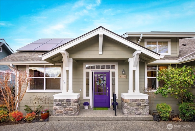 property entrance with stone siding, roof mounted solar panels, and a shingled roof