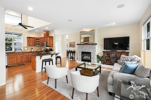 living area with recessed lighting, ceiling fan, a fireplace, and light wood finished floors