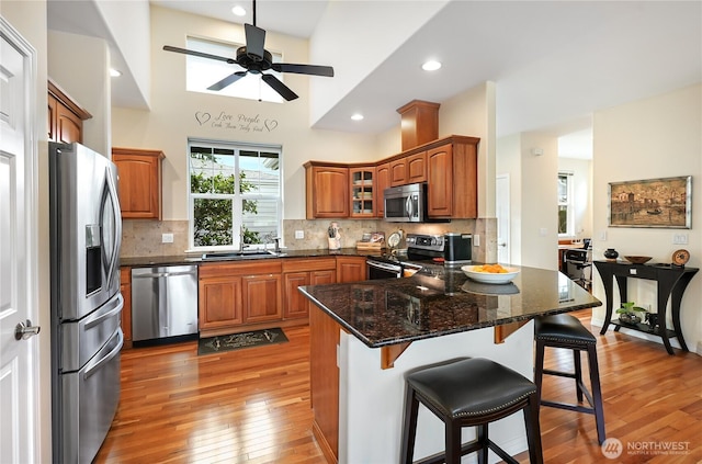 kitchen featuring brown cabinetry, light wood finished floors, a peninsula, stainless steel appliances, and a kitchen bar