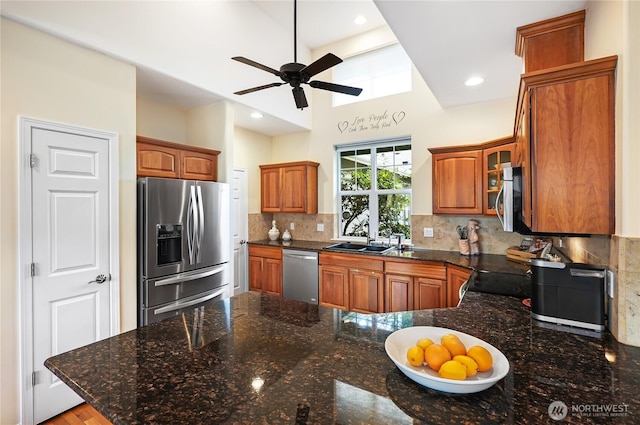 kitchen featuring brown cabinetry, a peninsula, a sink, decorative backsplash, and appliances with stainless steel finishes