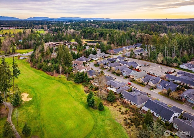 aerial view at dusk featuring a mountain view, a residential view, and a wooded view