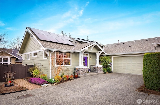 view of front of home with roof mounted solar panels, fence, concrete driveway, an attached garage, and a shingled roof