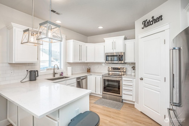 kitchen featuring appliances with stainless steel finishes, pendant lighting, sink, white cabinets, and kitchen peninsula