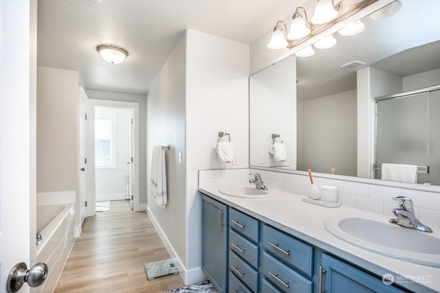 bathroom with wood-type flooring, a bath, decorative backsplash, and vanity