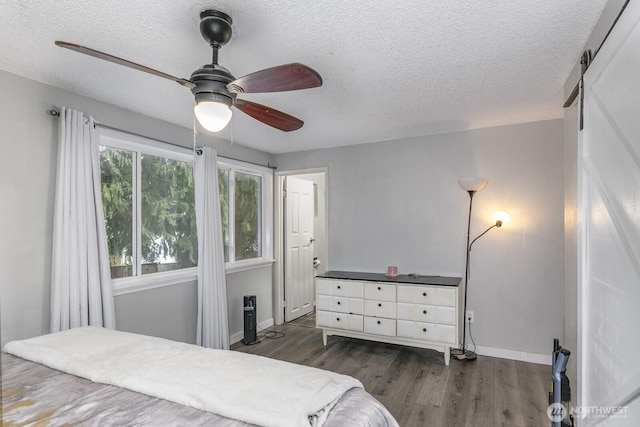 bedroom featuring ceiling fan, a barn door, dark hardwood / wood-style floors, and a textured ceiling