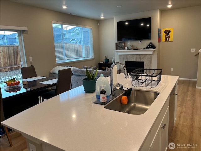 kitchen with sink, light hardwood / wood-style flooring, a wealth of natural light, white cabinets, and a tiled fireplace