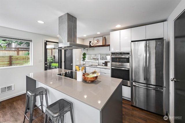 kitchen featuring a kitchen island, appliances with stainless steel finishes, island range hood, white cabinetry, and a kitchen bar