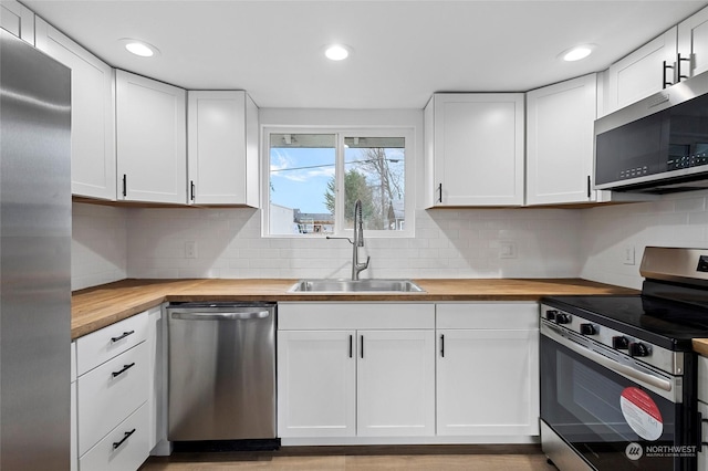 kitchen with sink, butcher block countertops, white cabinetry, tasteful backsplash, and stainless steel appliances