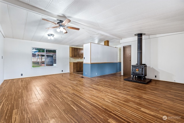 unfurnished living room with hardwood / wood-style floors, lofted ceiling with beams, ceiling fan, and a wood stove