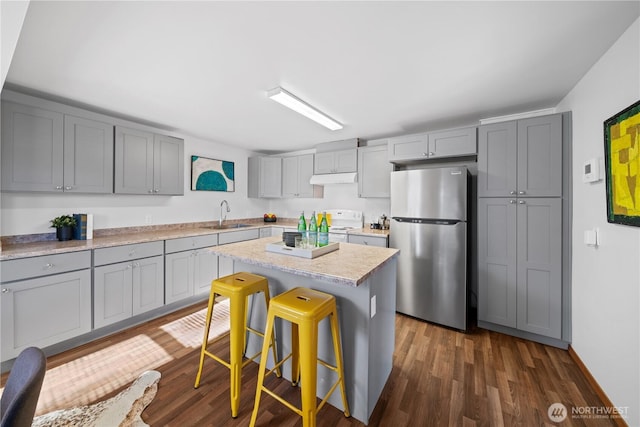 kitchen with sink, stainless steel fridge, gray cabinets, a kitchen breakfast bar, and a center island