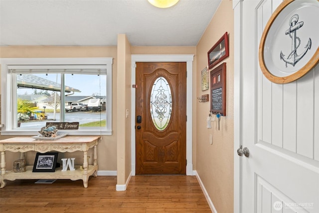 foyer featuring light wood finished floors, baseboards, and a textured ceiling