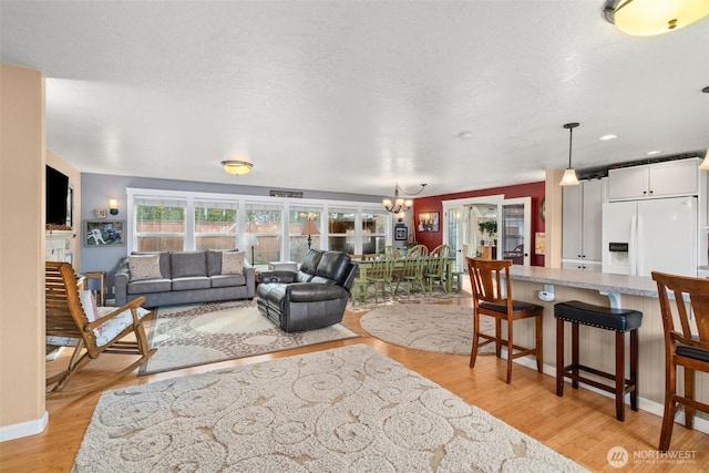 living area with a textured ceiling, light wood-type flooring, baseboards, and a notable chandelier