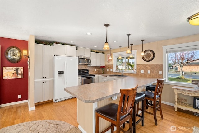 kitchen featuring appliances with stainless steel finishes, white cabinetry, a sink, a peninsula, and a kitchen bar