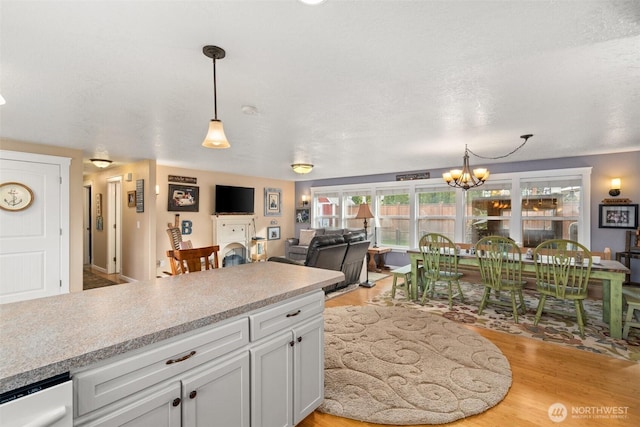 kitchen with decorative light fixtures, light countertops, light wood-style flooring, an inviting chandelier, and white cabinets