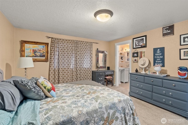 bedroom with a textured ceiling, ensuite bathroom, and light colored carpet