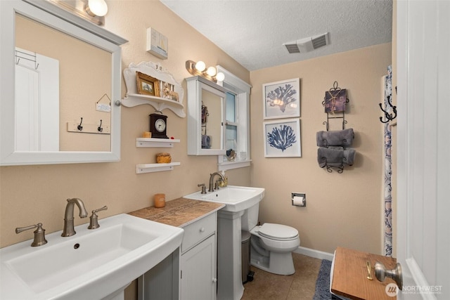 full bath with visible vents, two sinks, toilet, tile patterned flooring, and a textured ceiling