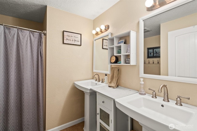 bathroom with a textured ceiling, a textured wall, a shower with shower curtain, and a sink