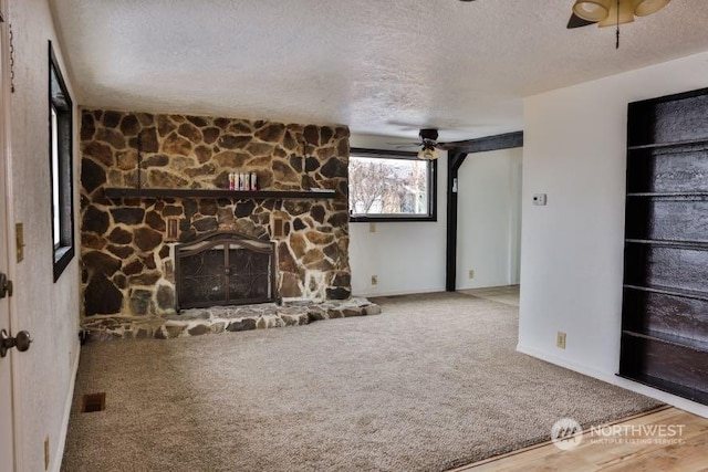 unfurnished living room with a stone fireplace, a textured ceiling, ceiling fan, and carpet flooring