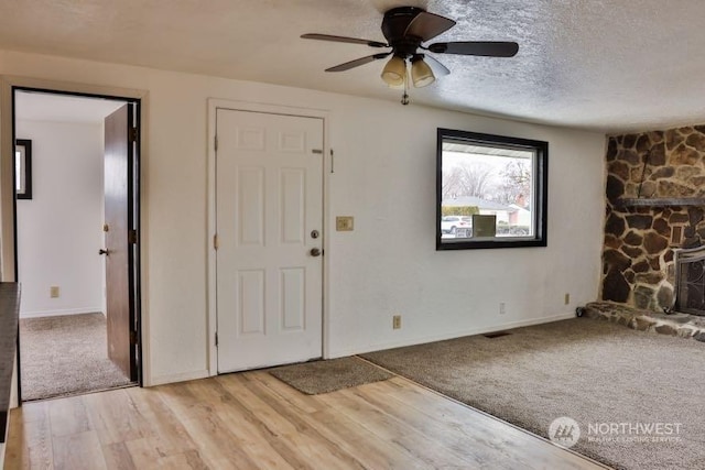 foyer featuring ceiling fan, a stone fireplace, light wood-type flooring, and a textured ceiling