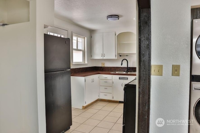 kitchen with sink, stacked washer / drying machine, white cabinets, and black fridge