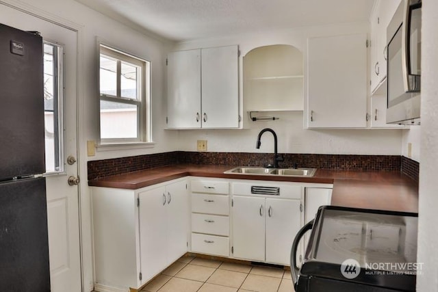 kitchen featuring sink, light tile patterned floors, range, black refrigerator, and white cabinets