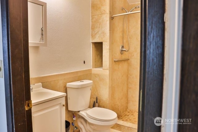 bathroom featuring tile walls, vanity, toilet, and tiled shower