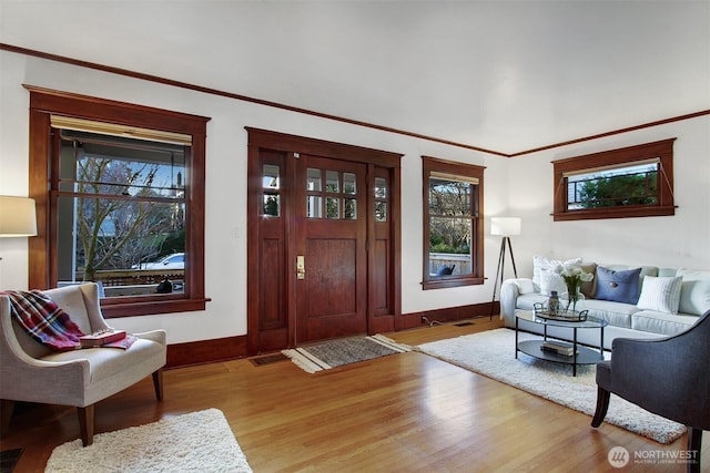 foyer with light wood-style floors, visible vents, baseboards, and crown molding