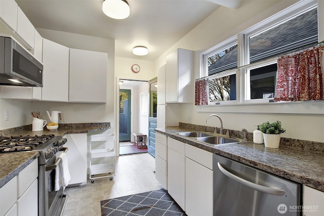 kitchen featuring dark countertops, stainless steel appliances, white cabinets, and a sink