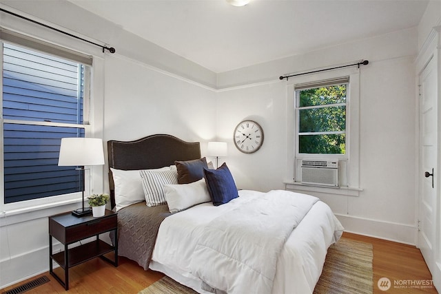 bedroom with cooling unit, visible vents, baseboards, and wood finished floors