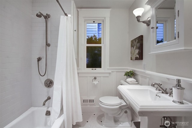 full bathroom featuring visible vents, wainscoting, toilet, shower / tub combo with curtain, and a sink