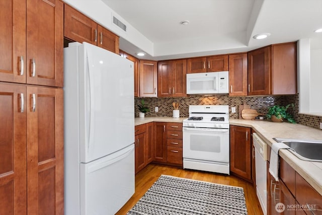 kitchen featuring white appliances, a tray ceiling, decorative backsplash, and light wood-type flooring