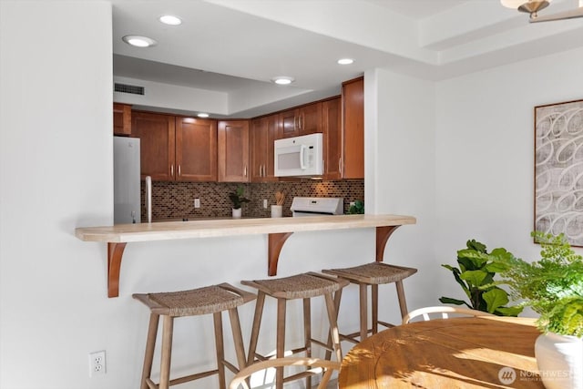 kitchen with a breakfast bar, stainless steel refrigerator, tasteful backsplash, stove, and kitchen peninsula