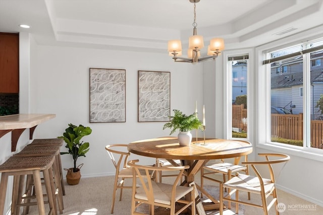 dining area with a raised ceiling, light carpet, and a chandelier