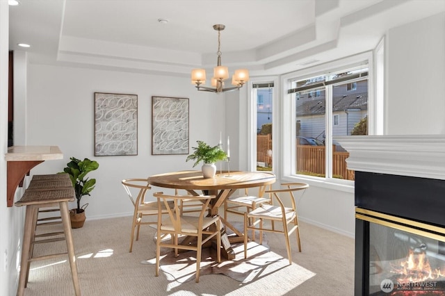 dining space with a raised ceiling, a multi sided fireplace, light carpet, and an inviting chandelier