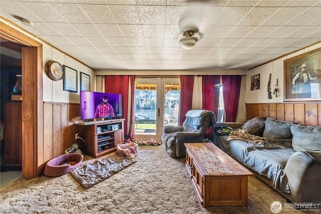 living room featuring wooden walls, french doors, and carpet flooring