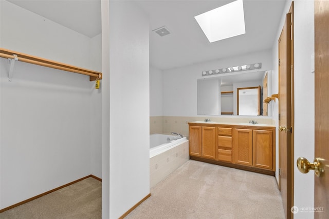 bathroom with tiled tub, vanity, and a skylight