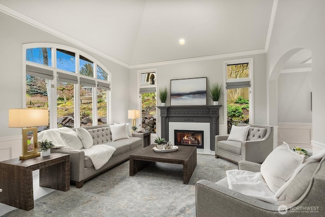 living room featuring crown molding, a glass covered fireplace, wainscoting, and plenty of natural light