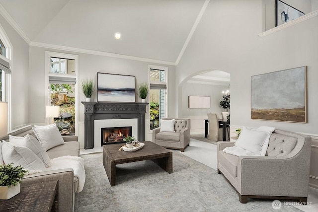 carpeted living room featuring high vaulted ceiling, arched walkways, a glass covered fireplace, and crown molding