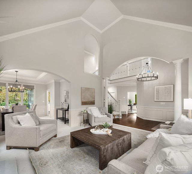 living room with arched walkways, crown molding, stairway, an inviting chandelier, and wainscoting