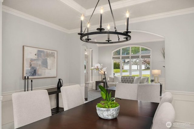 dining room featuring wainscoting, crown molding, a decorative wall, and a notable chandelier