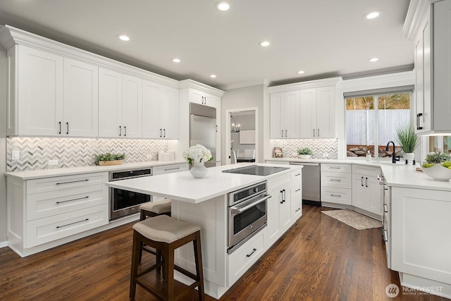 kitchen with a breakfast bar, a center island, stainless steel appliances, light countertops, and white cabinetry