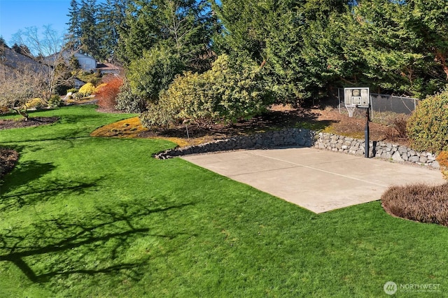 view of sport court featuring basketball hoop, fence, and a lawn