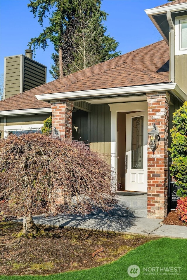 property entrance with brick siding, roof with shingles, and board and batten siding