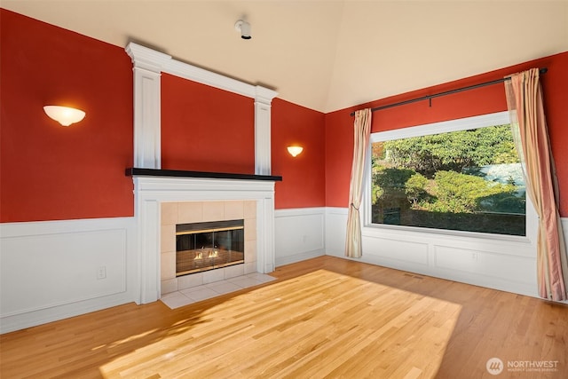 unfurnished living room featuring a wainscoted wall, a tiled fireplace, and wood finished floors