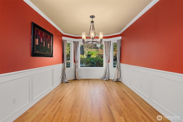 unfurnished dining area featuring a chandelier, light wood finished floors, a wainscoted wall, and ornamental molding